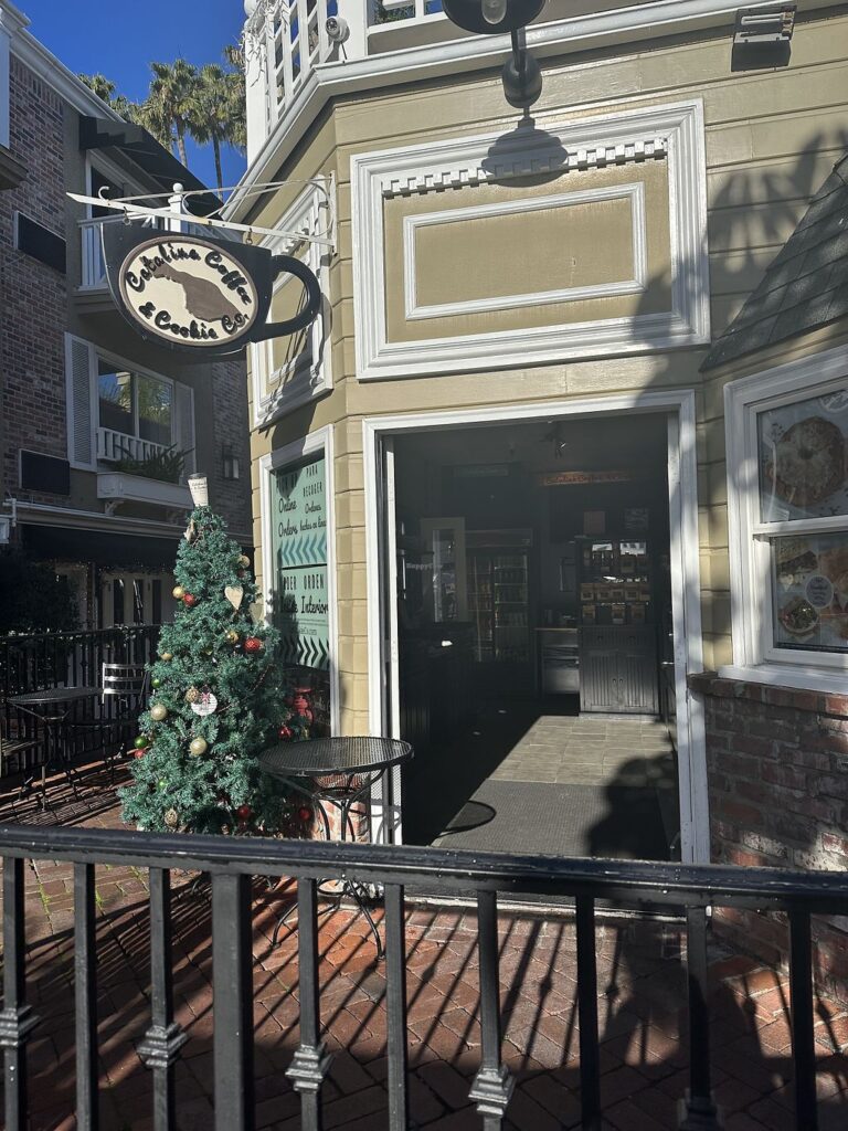 Exterior of Catalina Coffee & Cookie Co. in Avalon, with a hanging coffee-cup sign and a decorated Christmas tree by the entrance.